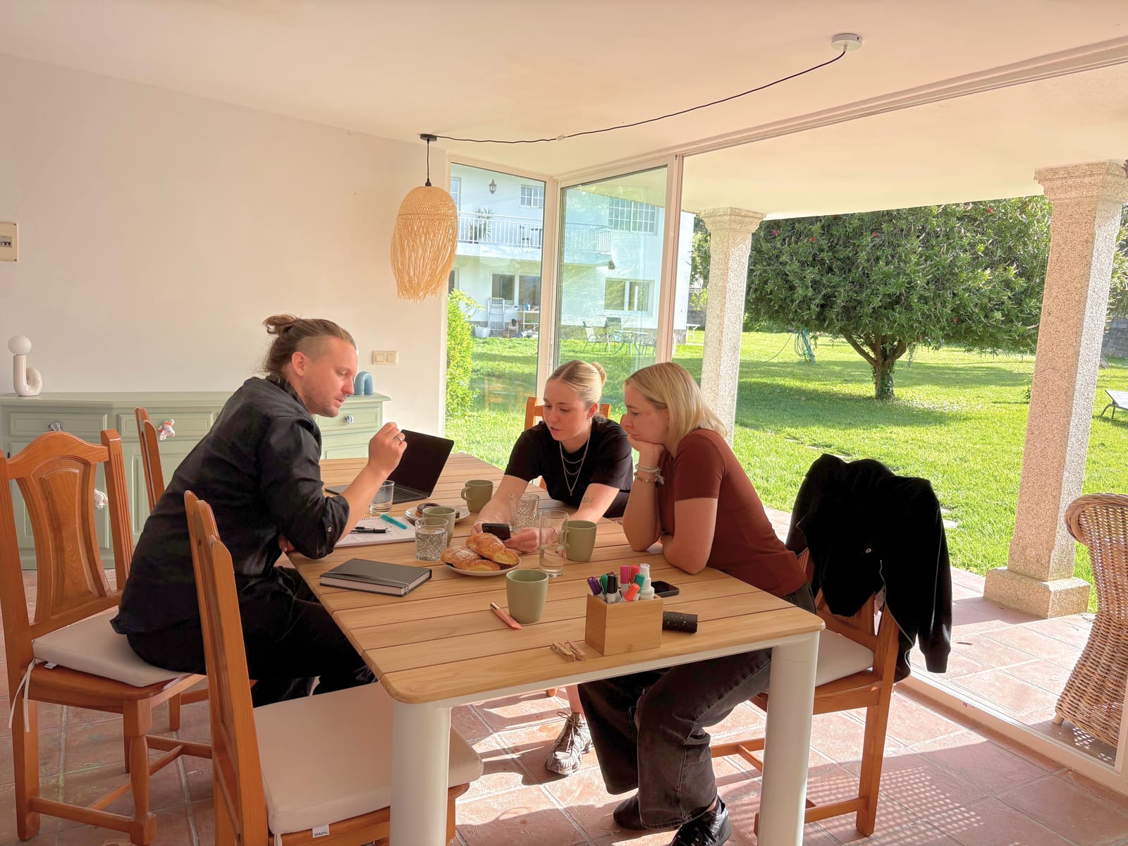 A small team working around the long table in the indoor workshop, with sliding doors open to the garden